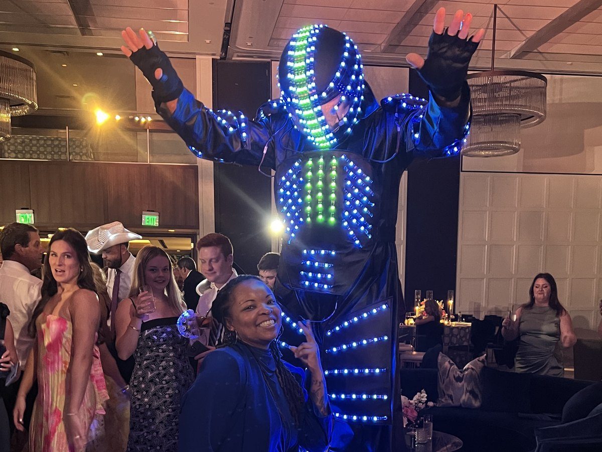 A performer in a towering LED-lit costume dancing with guests at a Carnival ball.