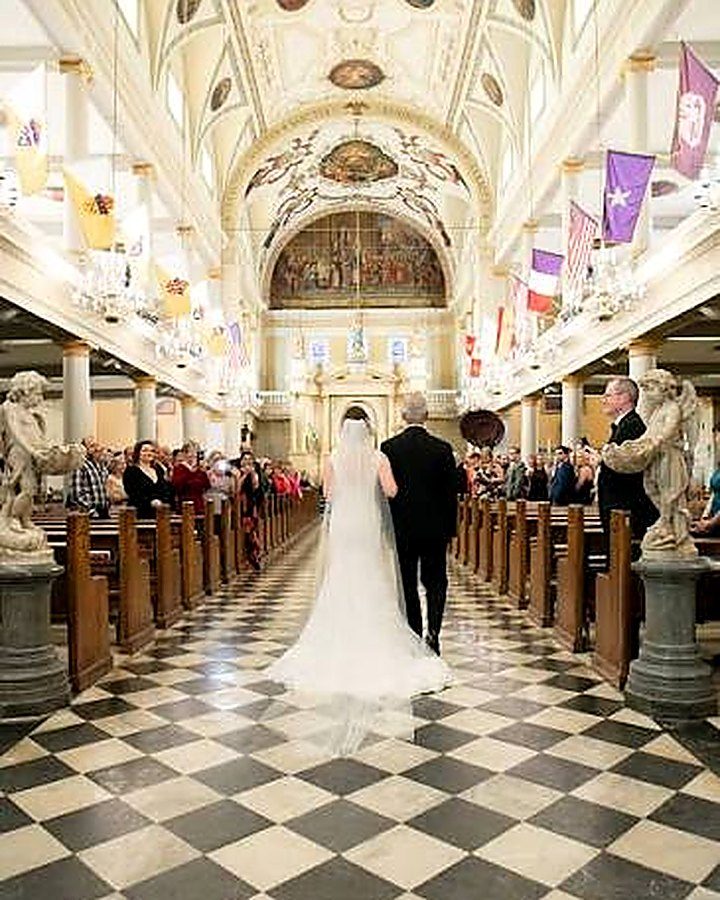 A bride and her father walking down the aisle of an ornate cathedral with a black-and-white checkered floor.