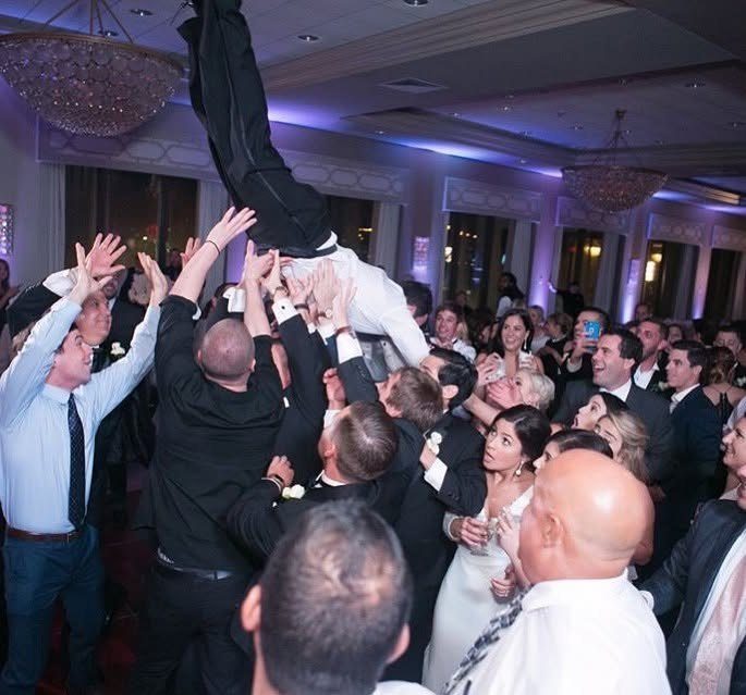 Wedding guests hoisting the groom above the dance floor in a ballroom.