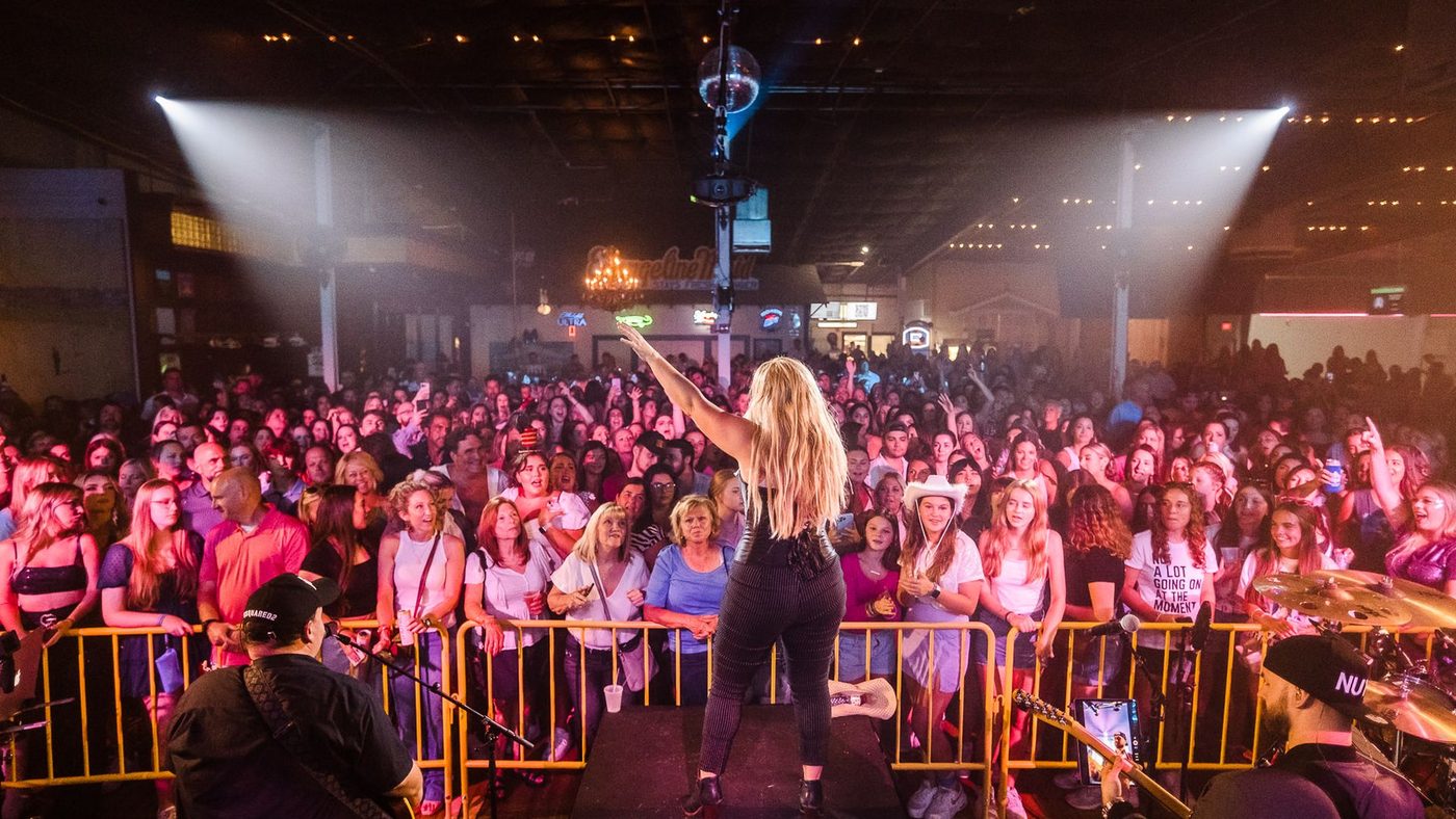 Britney vs Justin on an outdoor stage, the singer at the front lit by spotlights, a packed crowd at the barricade below.